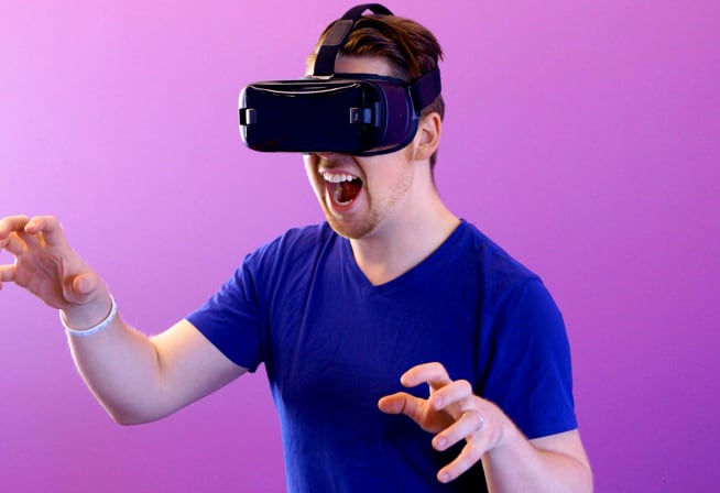 A man standing and wearing virtual reality goggles. He is posing as if he is growling with his hands extended as claws.